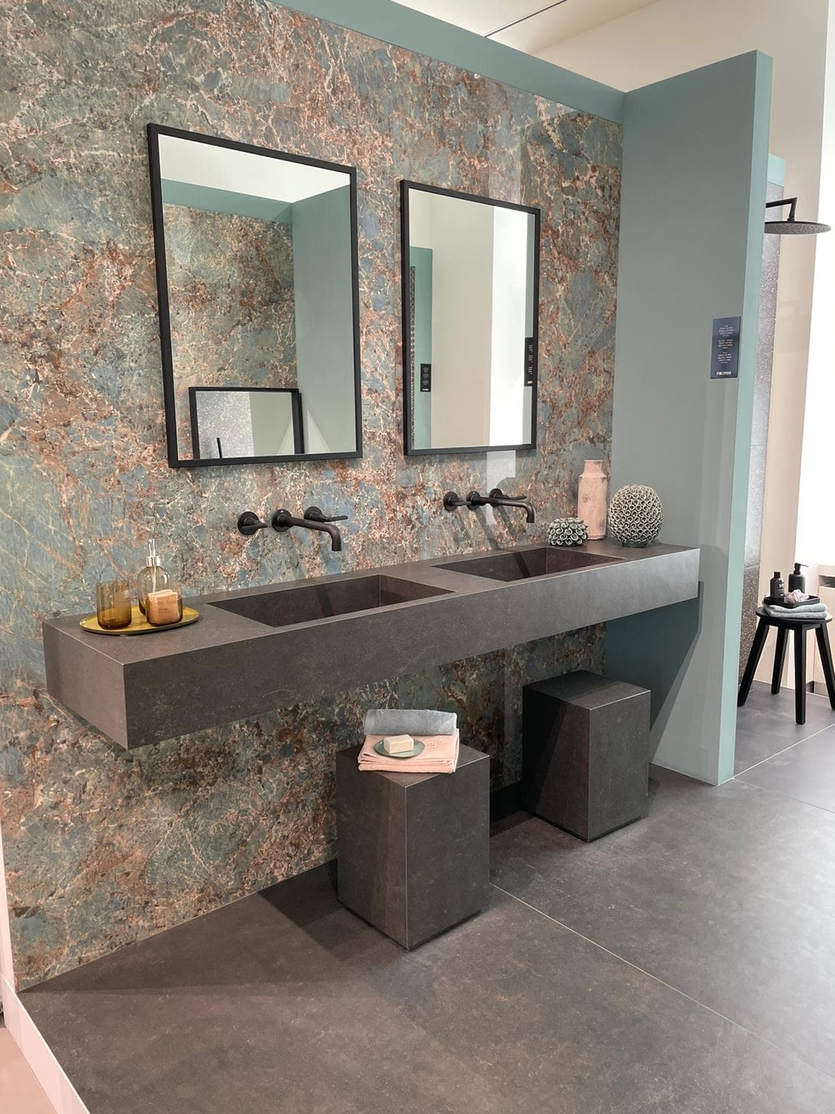 Zwei Spiegel in einem modernen Badezimmer mit grauem Doppelwaschbecken, grüner Wand und Dekoration.