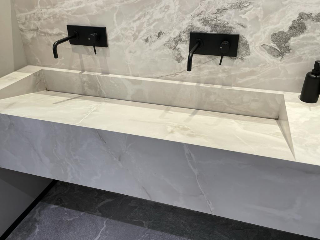 Ein elegantes, weißes Waschbecken mit marmorierter Rückwand und mattschwarzen Armaturen.